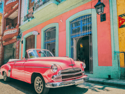 Vintage pink convertible taxi parked in front of colorful colonial buildings, capturing the essence of a Cuba group tour.