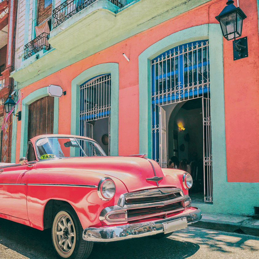 Vintage pink convertible taxi parked in front of colorful colonial buildings, capturing the essence of a Cuba group tour.