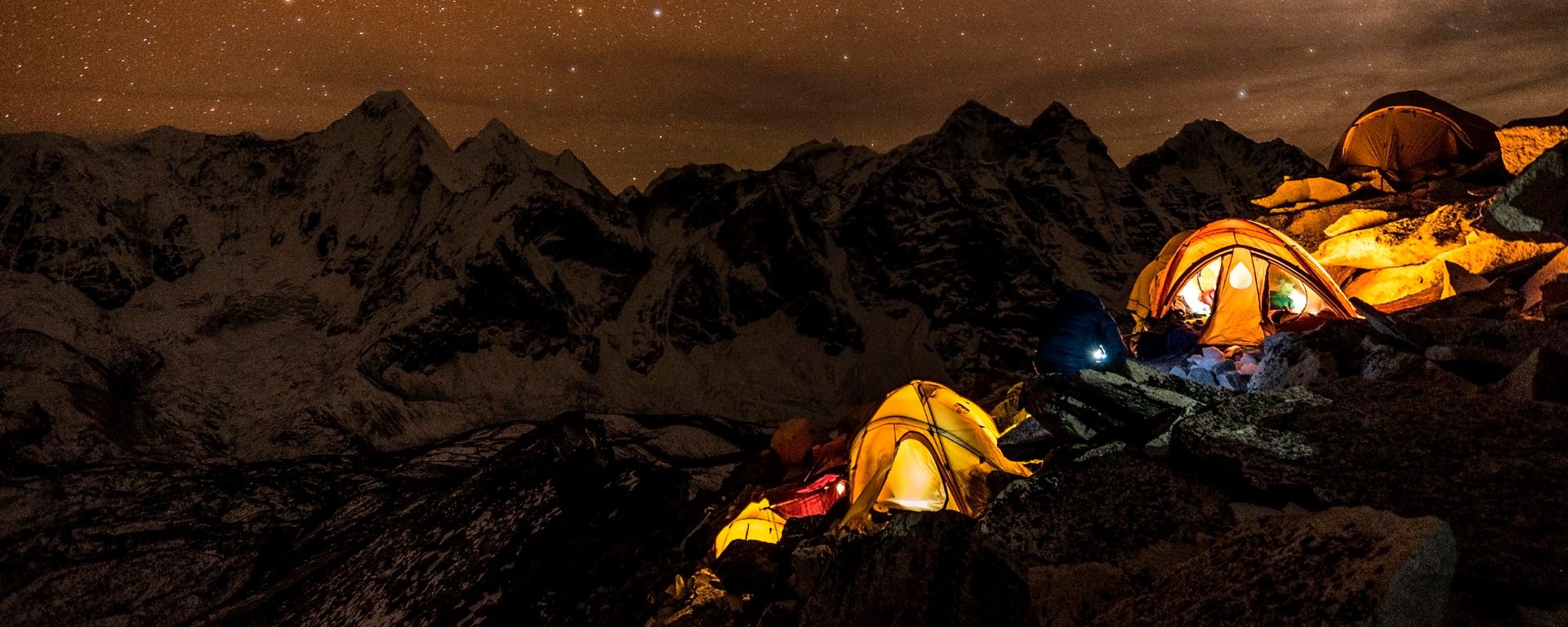 Tents illuminated at night under a starry sky in the mountains during a luxury hiking vacation.