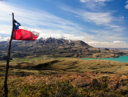 Chilean flag waving on a rugged mountain landscape with turquoise lakes, showcasing a scenic trip to Chile's National Parks.