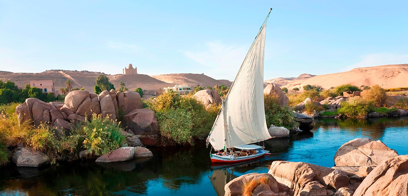 Traditional sailboat on a scenic Nile River cruise surrounded by lush greenery and desert landscapes.